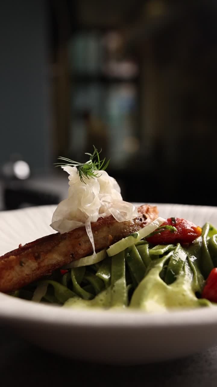 Chef's Hand Garnishing a Gourmet Pasta and Fish Dish