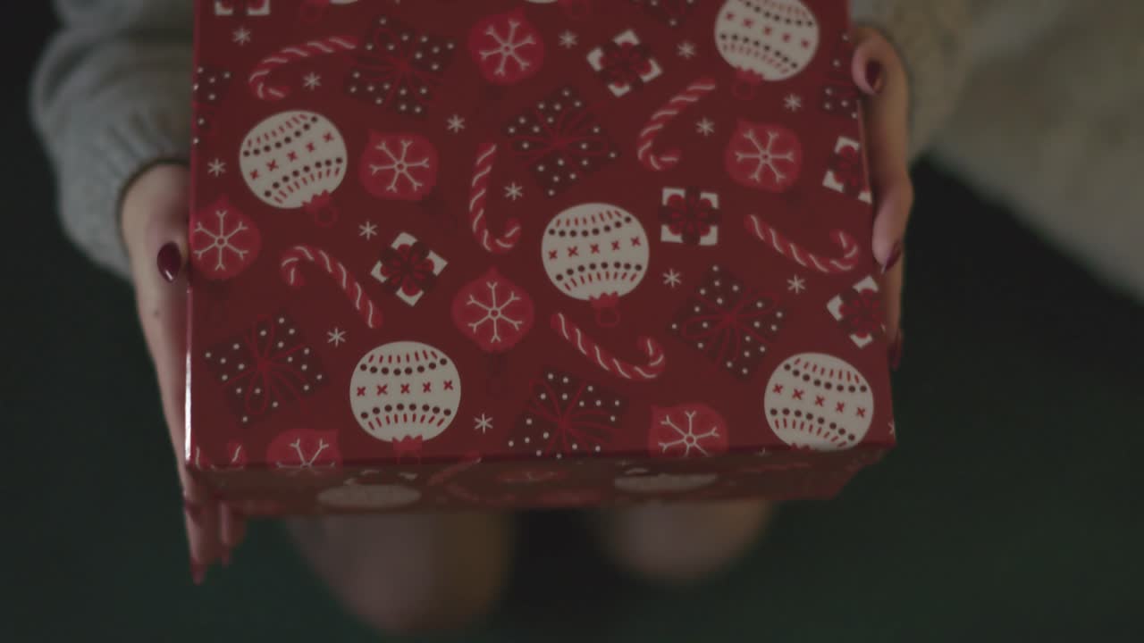 A close-up view of a wrapped Christmas gift box featuring red paper with white ornaments, candy canes, and snowflake patterns. The cozy holiday theme evokes warmth, joy, and the spirit of giving