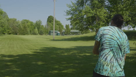 a man demonstrates the technique of a disc golf throw in an open grassy field on a sunny day, focusing on form and precision