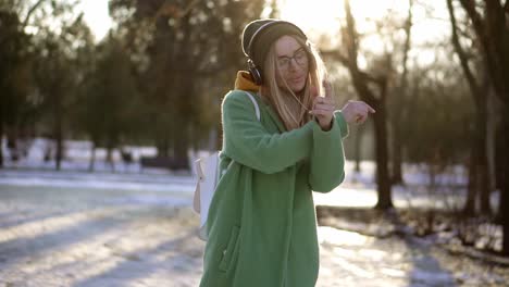 young woman dance freerly in winter park, listening to music on the phone using headphones