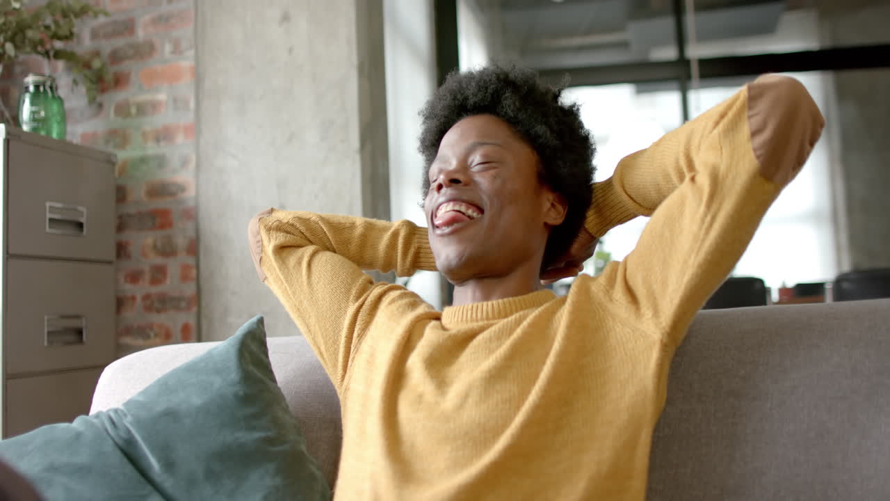 Happy african american man sitting on sofa and relaxing at home, slow motion