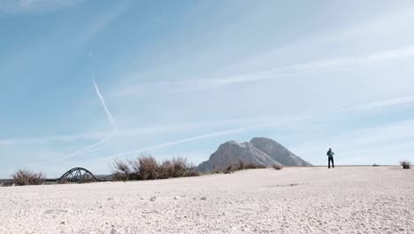 Person-walks-in-a-mountainous-landscape-with-clear-blue-sky-background