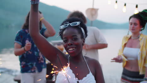 joyous black woman dancing with sparkler at lake party