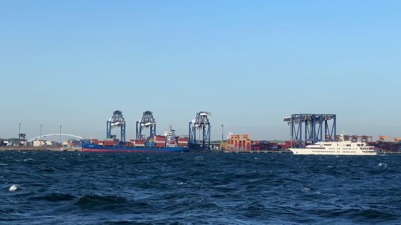 amplia fotografía de un bullicioso puerto marítimo con grúas y un barco de carga contra un claro cielo azul