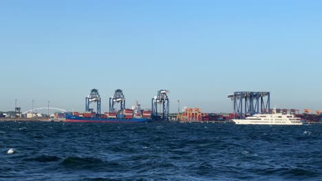 amplia fotografía de un bullicioso puerto marítimo con grúas y un barco de carga contra un claro cielo azul
