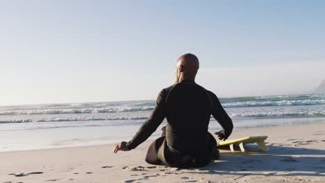 senior african american man sitting with a surfboard at the beach