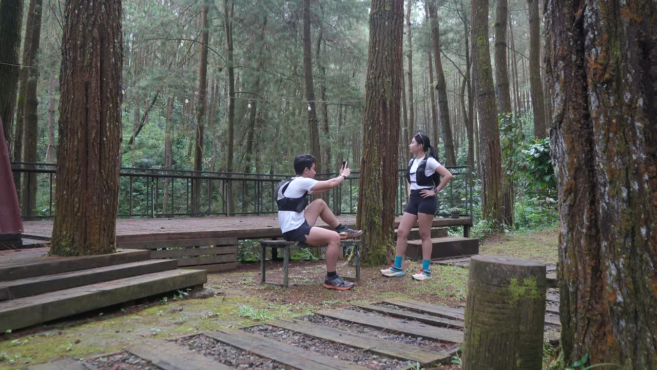 Asian couple taking photo with smartphone during outdoor trail run in Indonesian forest