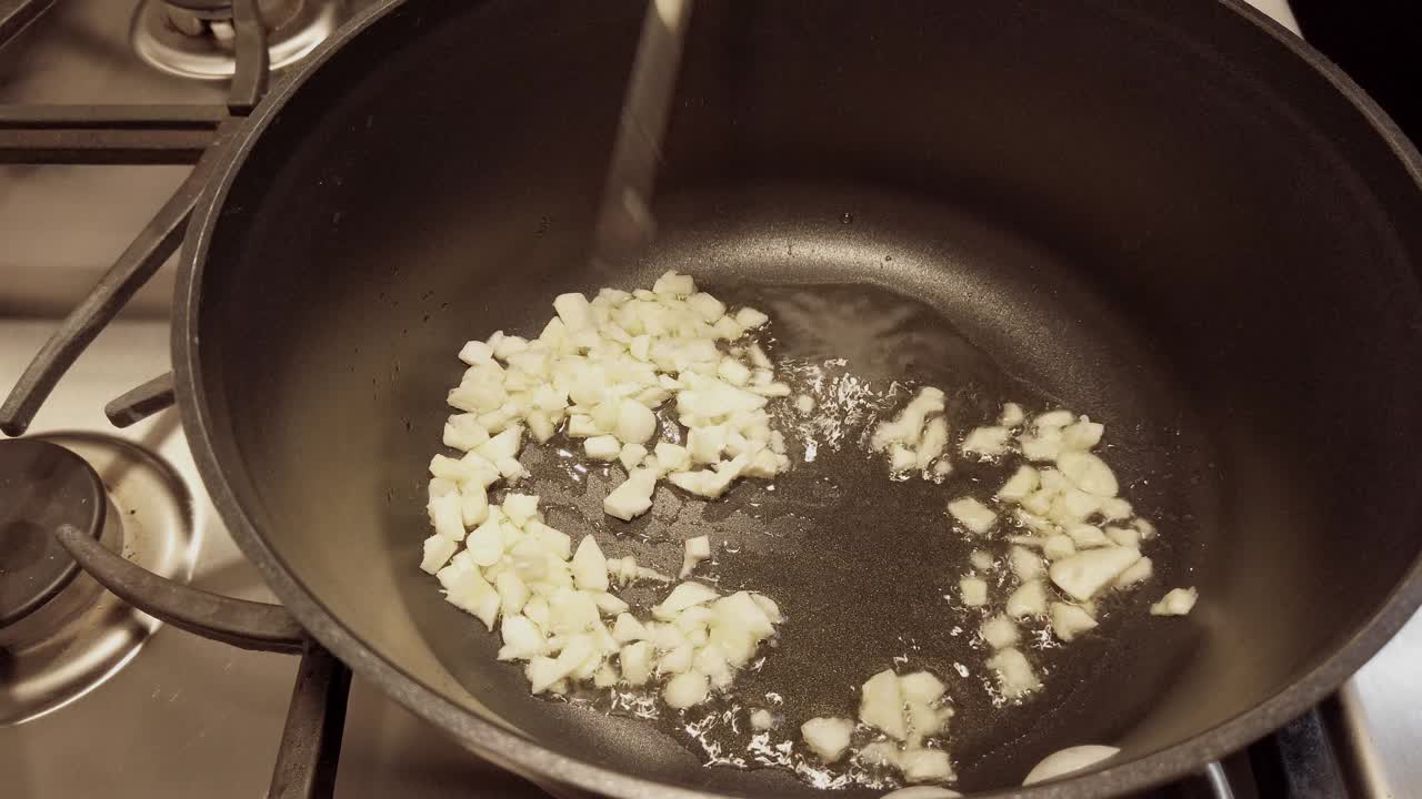 No person, non-stick pan adding chopped garlic to olive oil, side profile shot.