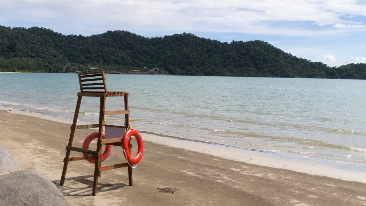 A quiet beach scene featuring an empty wooden lifeguard chair and rescue buoys by the water. Peaceful coastal atmosphere filmed at Blue Haven Bay on Koh Chang in Thailand