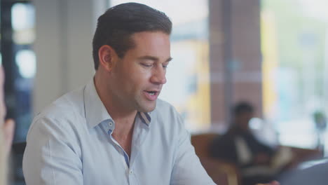 Close-Up-Of-Business-Team-Having-Meeting-Sitting-Around-Table-In-Modern-Open-Plan-Office