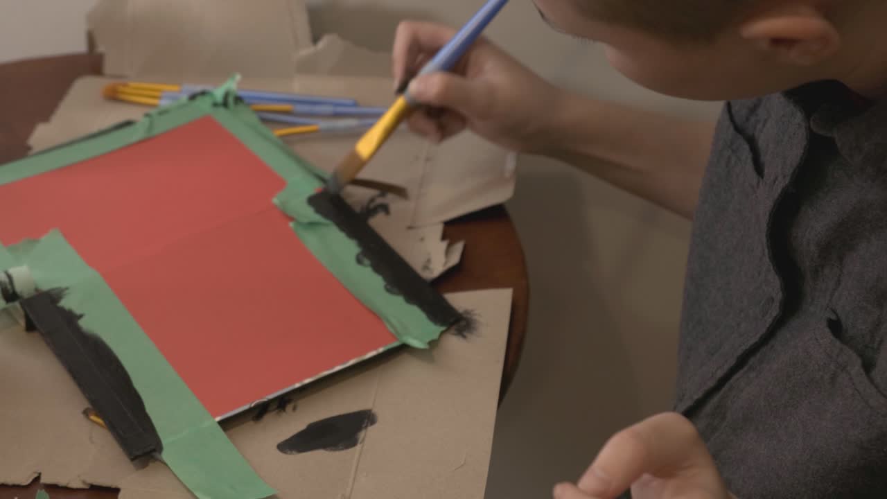 A Man Applying Black Paint To The Border Of A Red Board - Closeup Shot