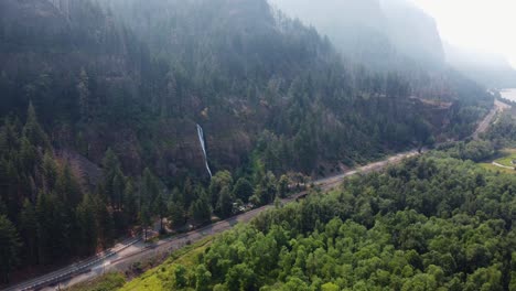 Drone-shot-of-a-road-in-the-Columbia-River-Gorge-with-Horsetail-Falls-majestically-cascading-over-the-cliffside