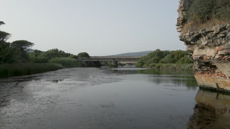 Drone-shot-low-flying-forwards-passed-an-old-roman-ruin,-flying-over-calm-waters-of-a-river-in-Southern-Spain