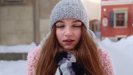 una chica viajera sonriente se frota las manos con guantes tratando de mantenerse caliente en el clima helado en la calle de la ciudad