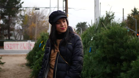 A-hispanic-woman-shopping-for-a-seasonal-holiday-Christmas-tree-decoration-on-a-lot-with-many-species-of-festive-trees