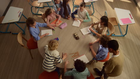 kids sitting at round table at school. diverse students preparing for lesson