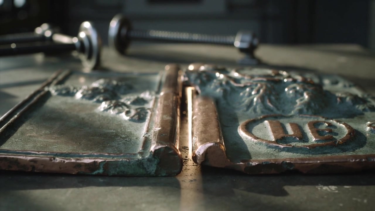 Telecamera che si sposta mostrando pannelli metallici in rilievo su una panca, per evidenziare patina, cerniera, morsetto, asta.