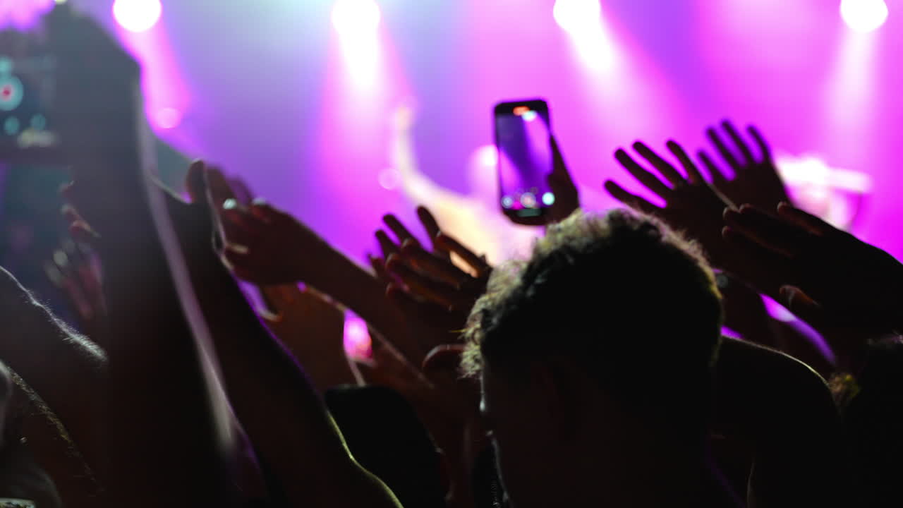 Concertgoers raising hands, generating vibrant energy through colorful stage lighting during powerful live music performance, capturing collective excitement and unity