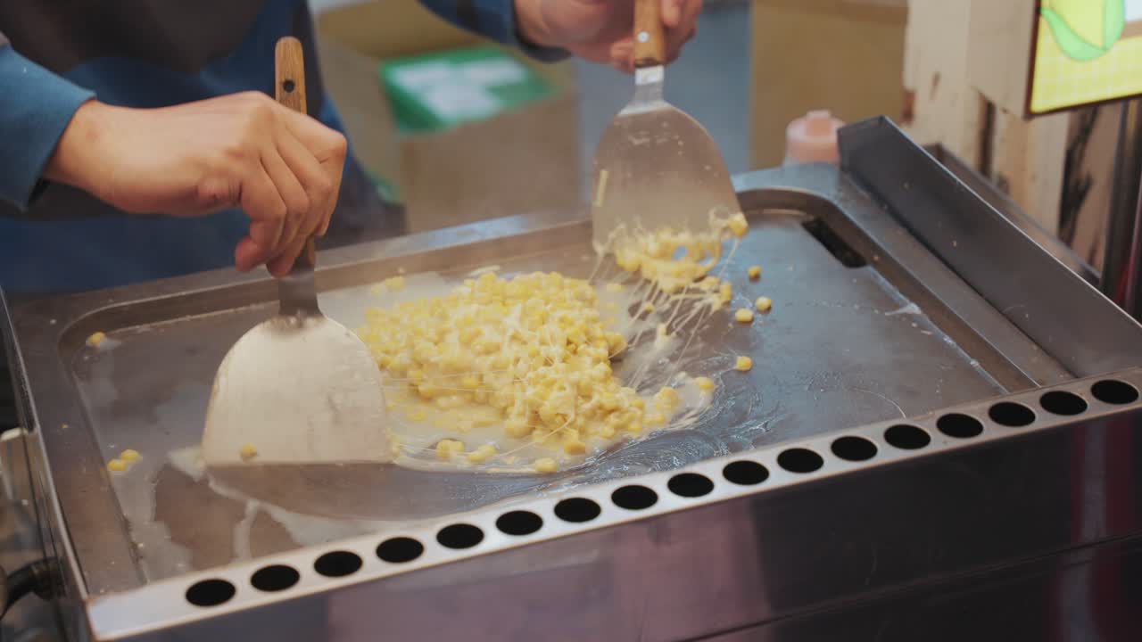 A look at Taiwanese street food as a vendor grills cheesy corn to perfection, blending creamy toppings with smoky flavors in a bustling night market setting