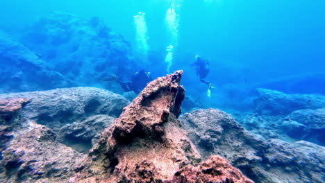 snorkel divers with scuba gear swimming underwater on the rocky sea floor