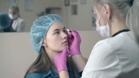 el cosmetólogo hace marcas en la cara de la chica para el maquillaje permanente