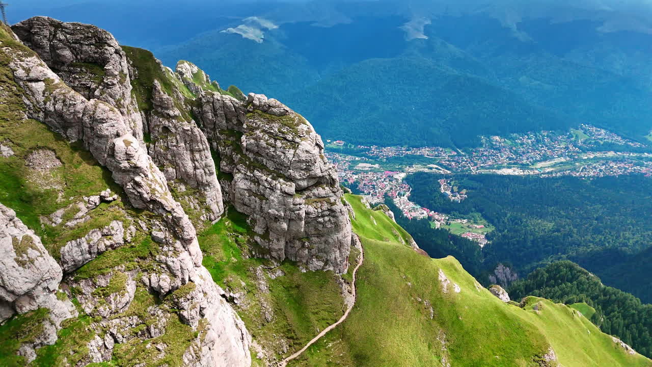 Grey cliffs covered with green grass. Spectacular scenery of the village at the mountain foot. The Bucegi Mountains, Romania