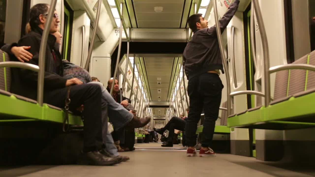 People utilizing Spain's public transportation system via subway in Europe, couple sits down enjoying ride and talking to each other, man stands up