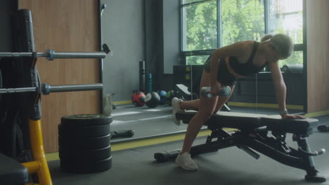 woman doing dumbbell bench rows in gym