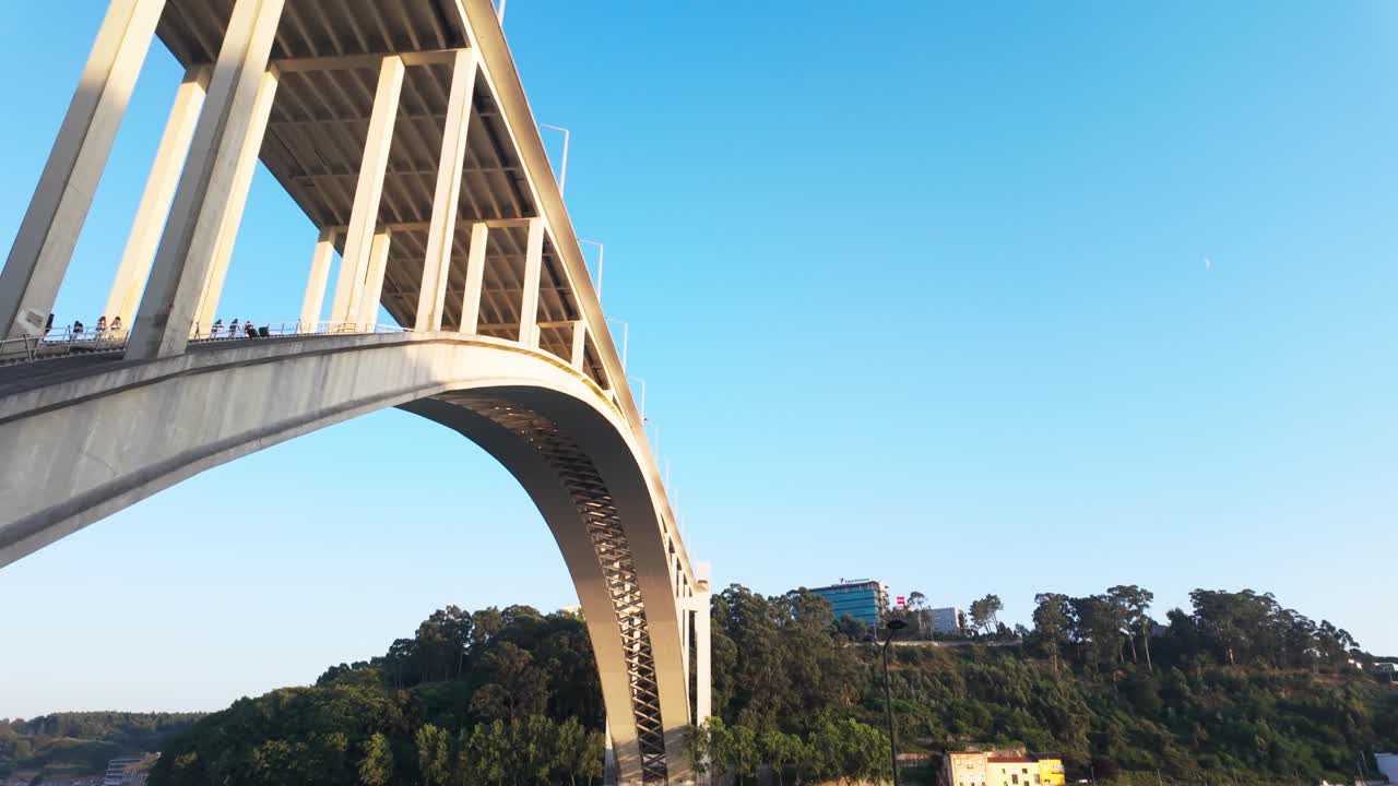Walking path beside the Arrábida Bridge in Porto, bordered by wooden fencing and greenery