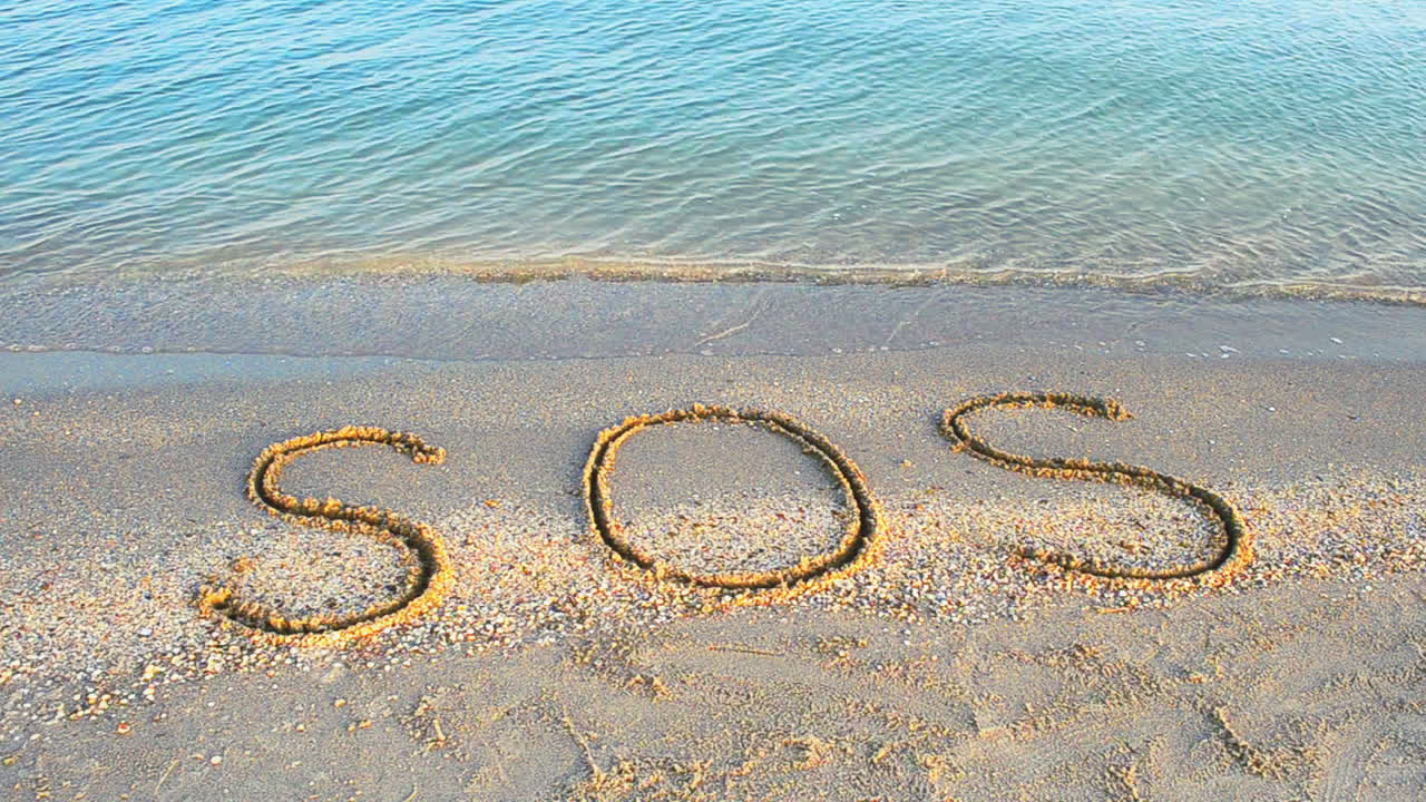 Kum üzerine yazılmış SOS yazısı. Sahilde çekim