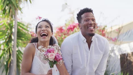 happy married african american couple with flowers wearing wedding clothes