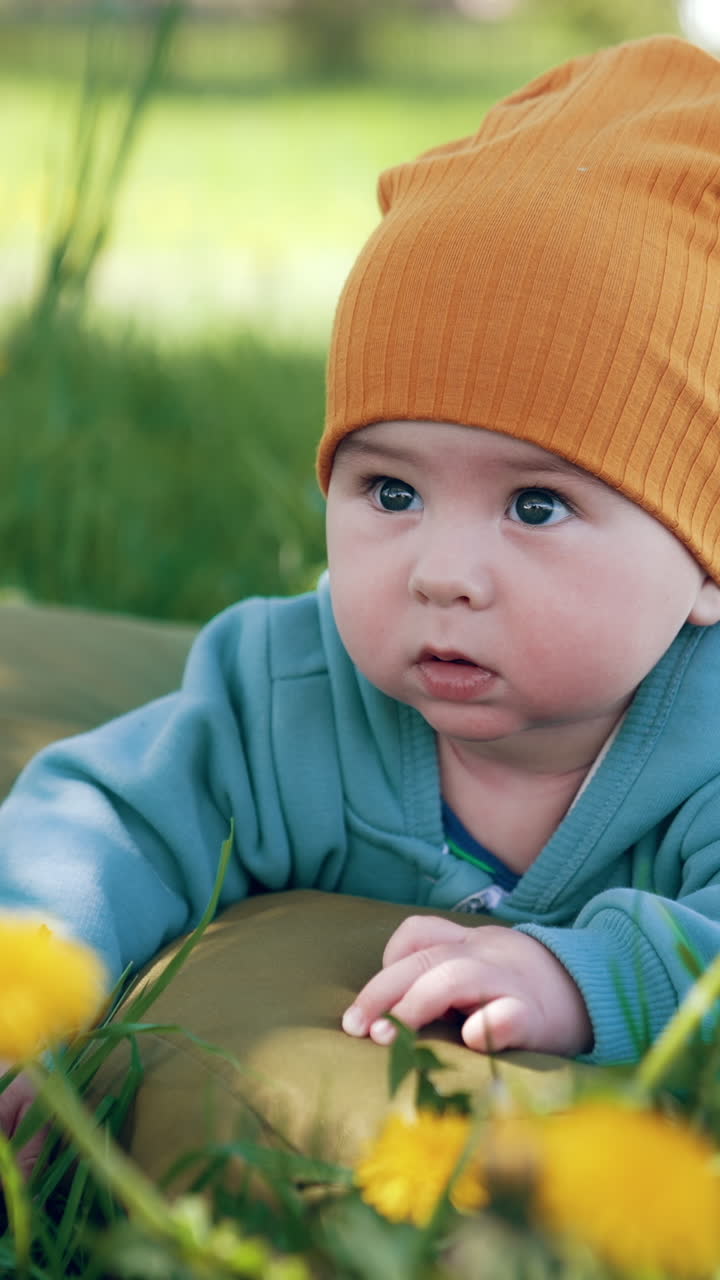 Cute toddler lying on the mattress in the grass with dandelions. Adorable baby looks up smiling sweetly. Vertical video