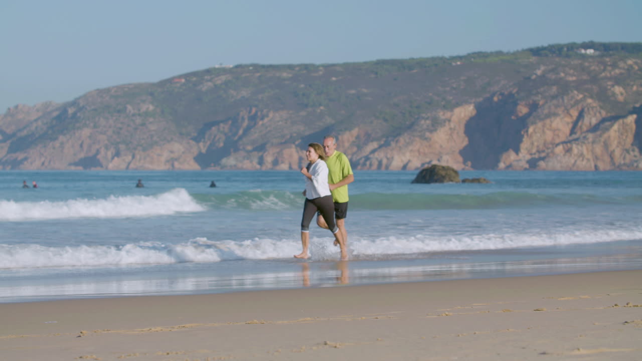 una feliz pareja madura corriendo descalza en la playa de arena