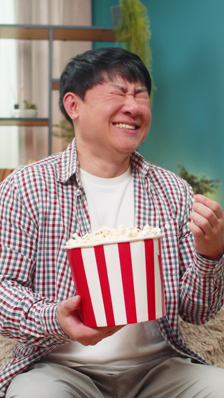 Asian man laughing loudly watching comedy movie eating popcorn joyful relaxed mood hearty laughter