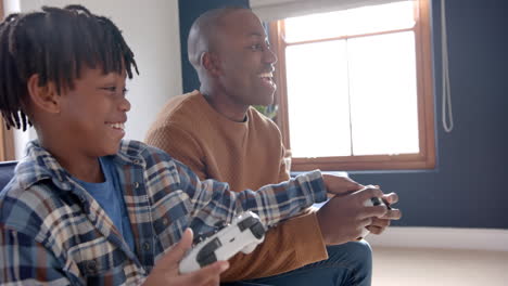 happy african american father and son playing video games and fooling around at home, slow motion