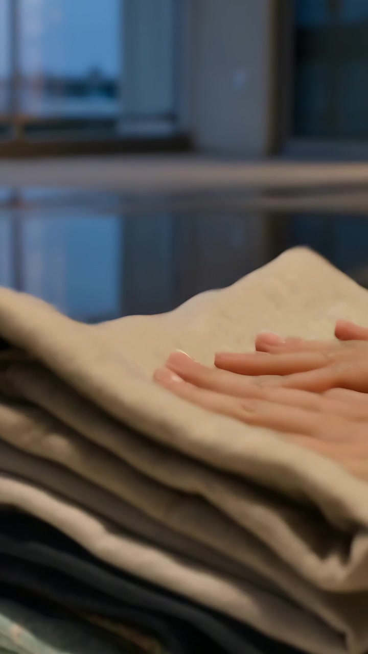 Vertical video: Entering hand from right, stacking folded towels on glossy balcony surface, tidying