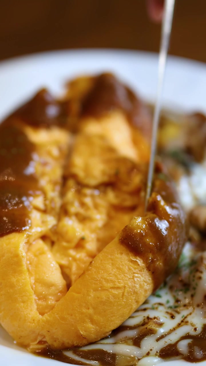 Primo piano di omurice che viene affettato, rivelando un interno cremoso, sotto una luce calda in un ambiente da ristorante.