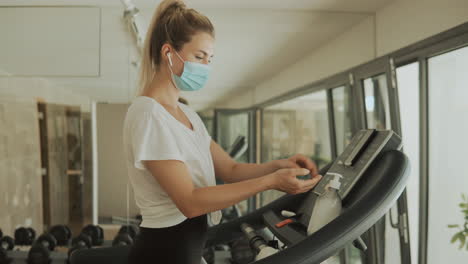 young athlete female with face mask uses an exercise machine and hand sanitizer in the gym