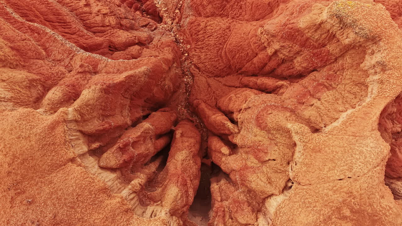 Paesaggio di canyon con formazioni rocciose rosse e terreno accidentato, con texture e motivi visibili, a mezzogiorno sotto un cielo sereno.