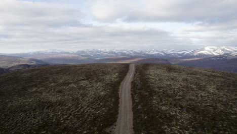 cinematic aerial drone footage flying up and over wild heather, grouse moorland and lichen heath to reveal a mountain landscape with patches of snow and clouds