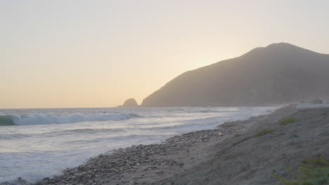 plan fixe au ralenti de vagues courant le long des rives de la plage de mondo alors que le soleil se couche derrière la montagne située dans le sud de la californie