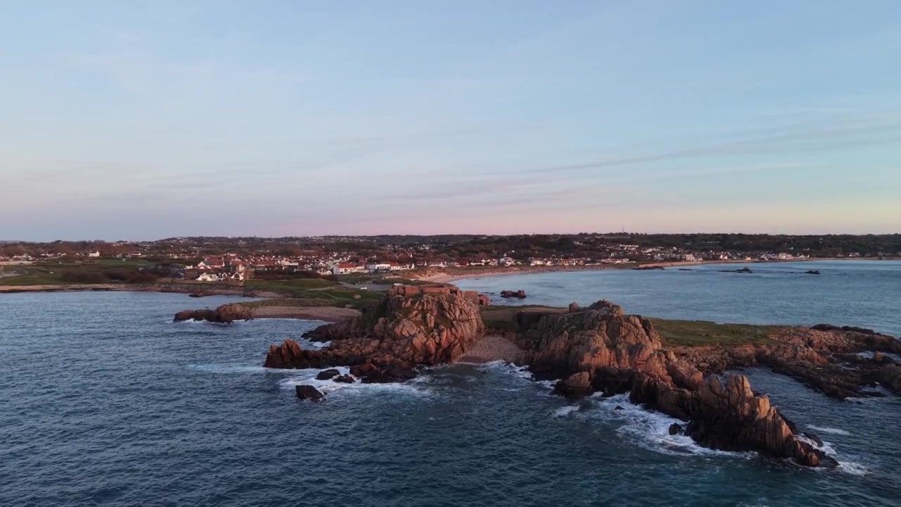 Grandes Rocques, Guernesey, Îles Anglo-Normandes. Images de drone révélant à l'heure dorée un ancien fort militaire au-dessus d'une eau bleue claire et de rochers avec des vagues déferlantes, ainsi que de magnifiques baies et plages sur la côte ouest