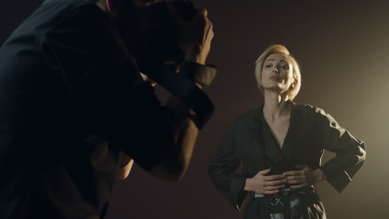 사진 작가가 그녀의 사진을 찍는 동안 어두운 스튜디오에서 포즈를 취하는 백인 젊은 여성 모델