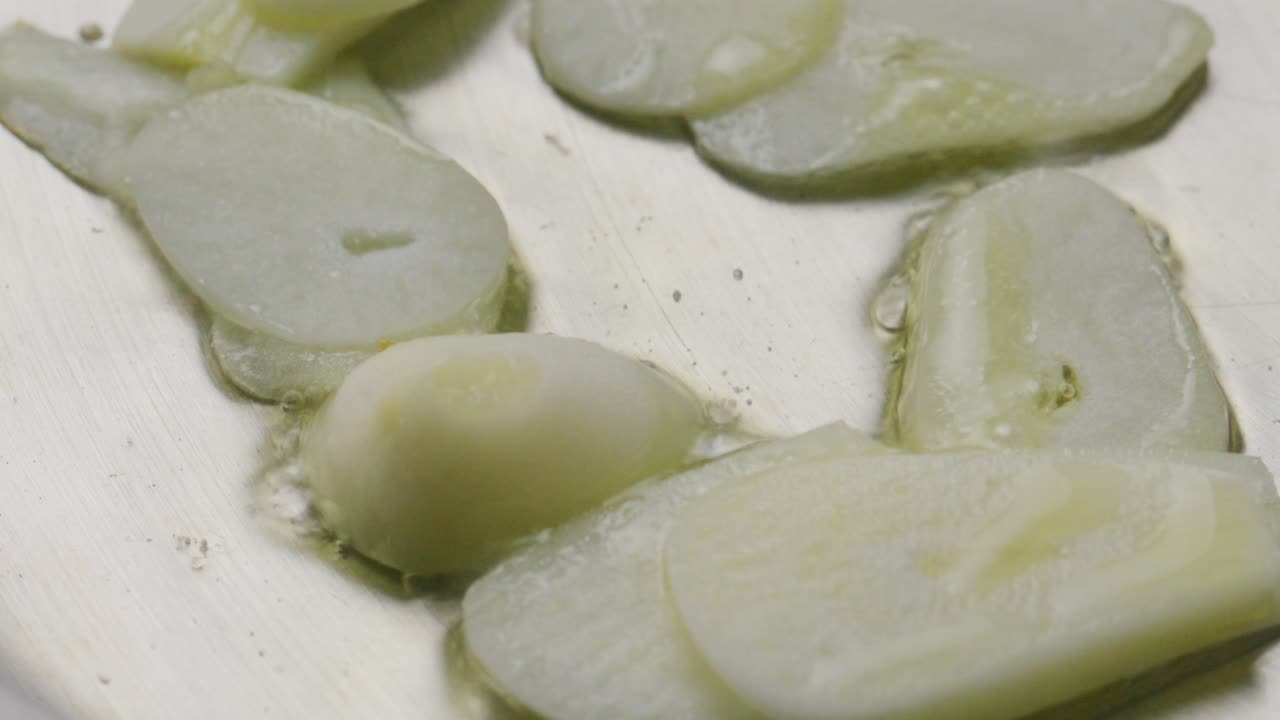 Slices of Garlic Sizzling in Oil in Metallic Frying Pan during Cooking