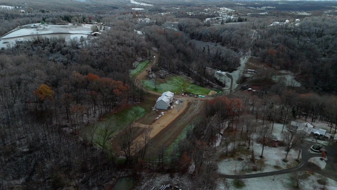 Cirkulär flygvy över en lerig gård i snöiga Morgantown, West Virginia, där en slingrande väg går genom en lövfri skog.