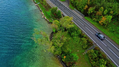 Vista-Aérea-De-Automóviles-Circulando-Por-Una-Carretera-Junto-Al-Lago-Flanqueada-Por-Coloridos-árboles-Otoñales