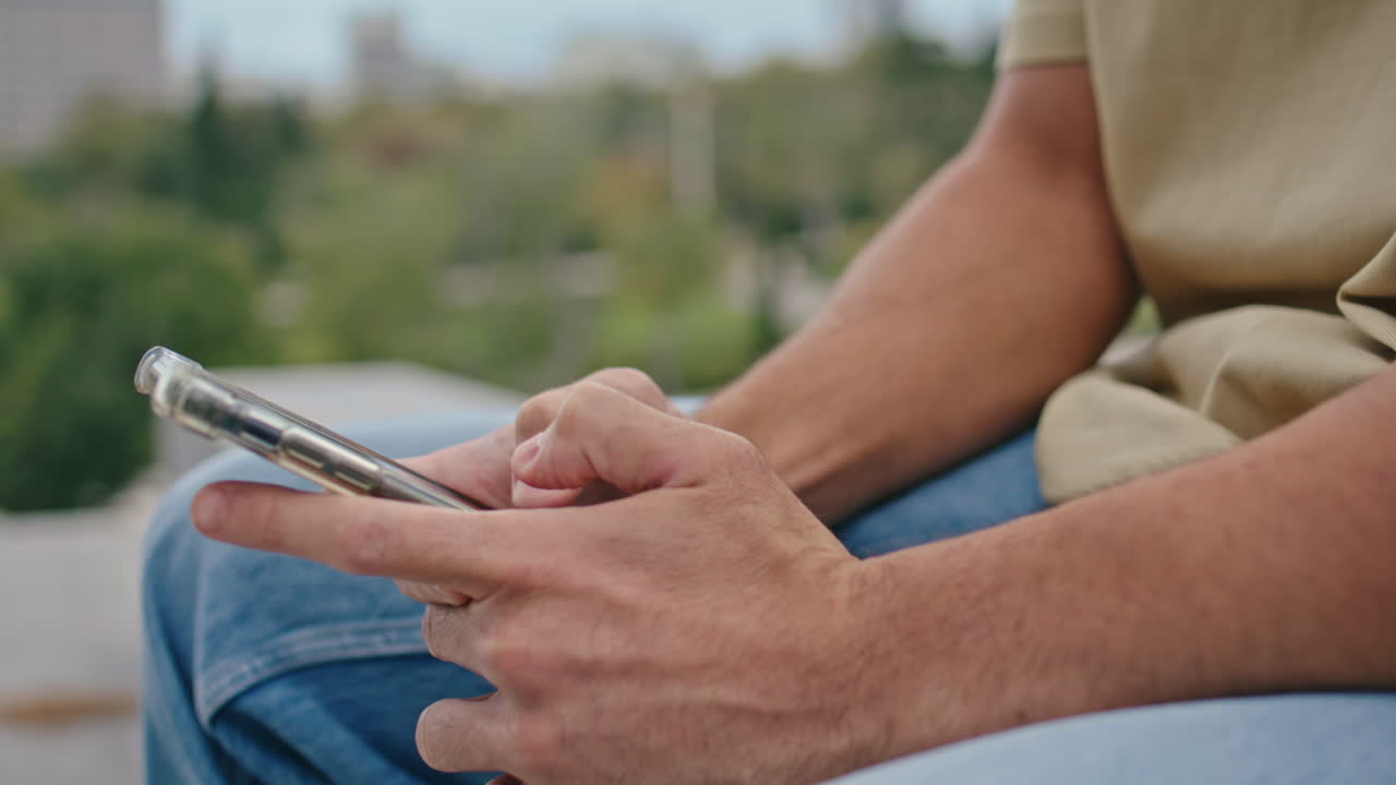 Mani di un uomo digitano un SMS sullo smartphone in un parco verde, in primo piano. Uomo sconosciuto che messaggia.
