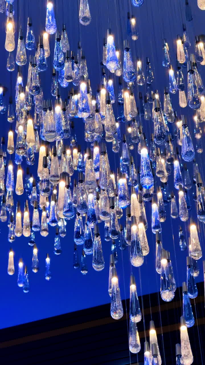Unusual blue and white bulbs hang on diverse levels. Low angle view at the beautiful decorative illumination. Vertical video.