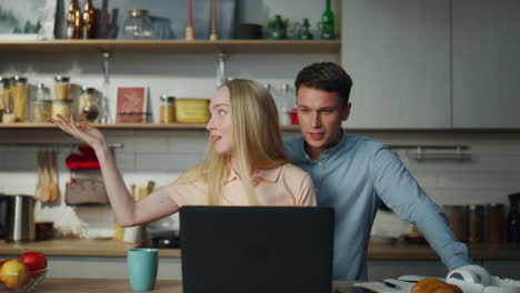 una pareja hablando por video en una computadora portátil en la cocina. una familia sonriendo hablando en línea.