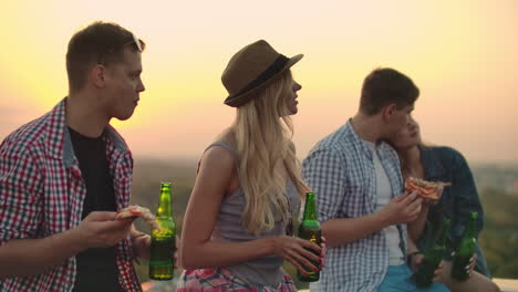 two couples in love eat pizza and drink beer on the roof. girls shyly look at their boyfriends. in one couple the girl laid her head swiftly on the shoulder of her young man.